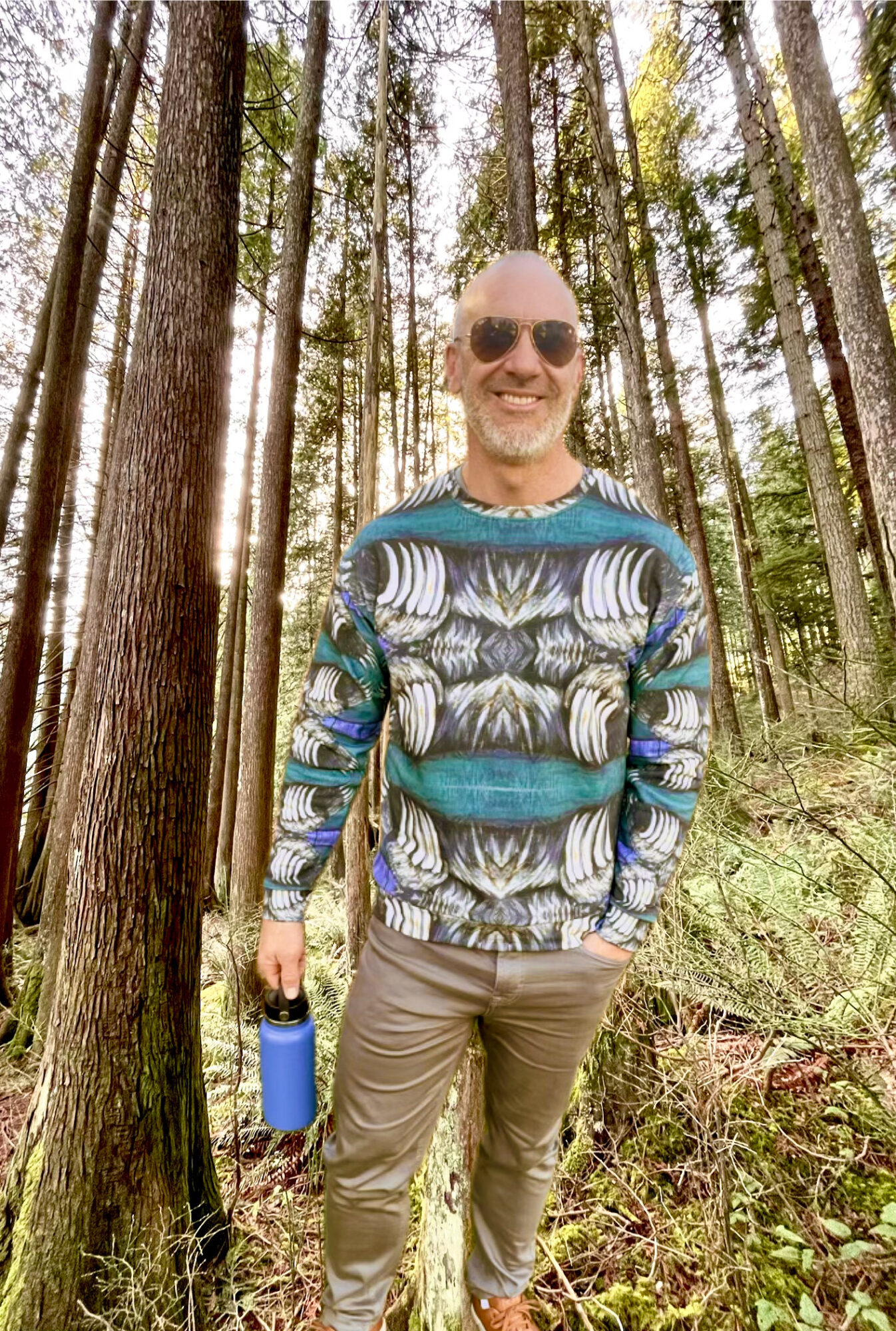 Model in the Bear Claw Sweatshirt by Tanya Tee Art standing by a West Coast lake and evergreens, showcasing the hand‑painted bear claw design.