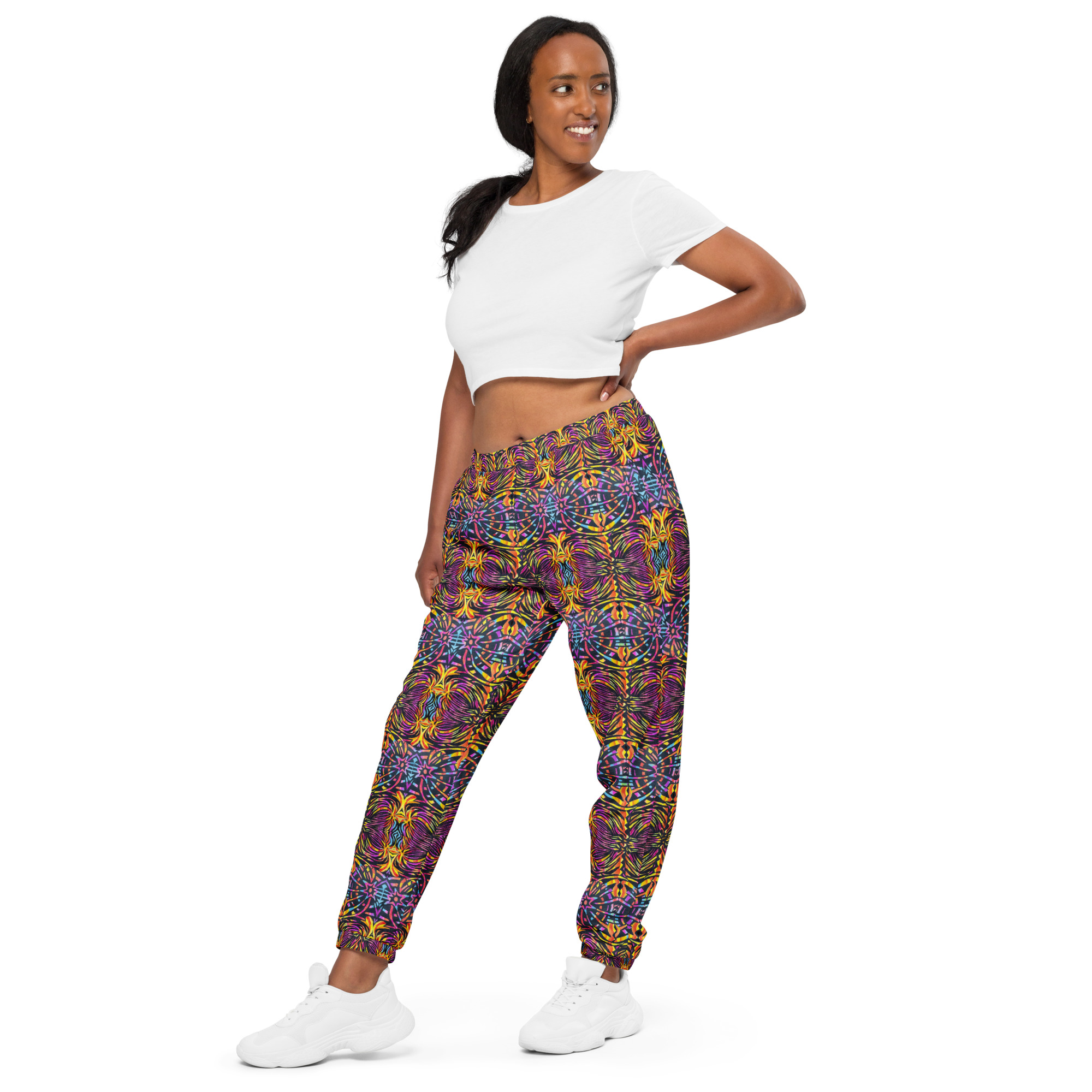 Person wears white shirt, and bold multicolored geometric pants against a plain white background.