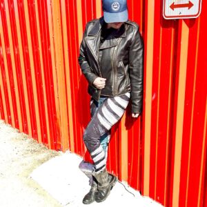 Model wears striking teal green, black and white pattern leaning on a red metal wall. Model size XL. Bear Claw Strike yoga pants with sculptural claw‑mark pattern in teal green, grey, and white”