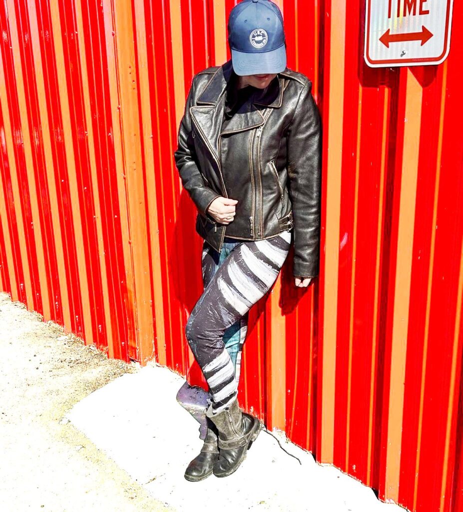 Model wears striking teal green, black and white pattern leaning on a red metal wall. Model size XL. Bear Claw Strike yoga pants with sculptural claw‑mark pattern in teal green, grey, and white”